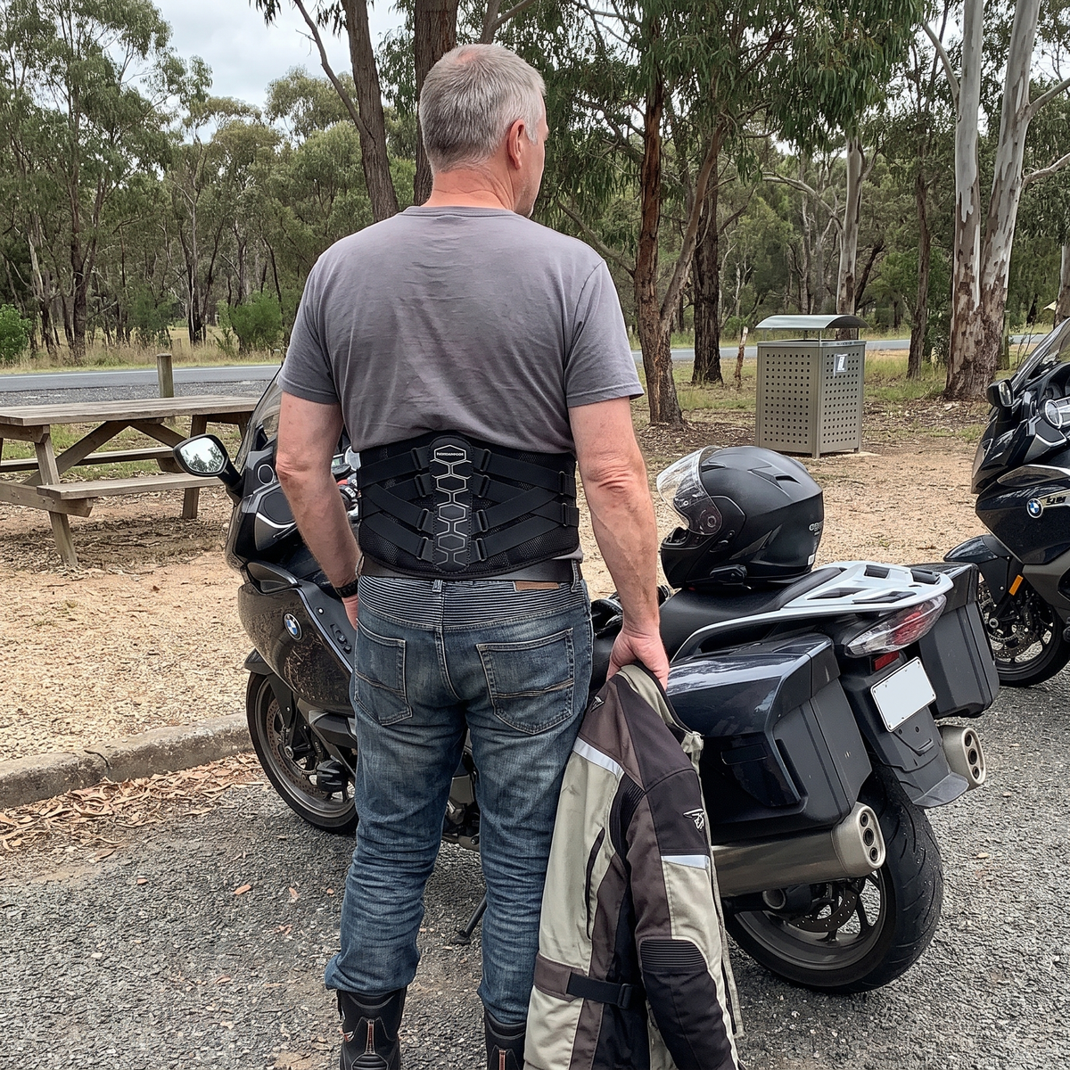 Rider at a roadside rest area wearing MotoSupport, jacket in hand